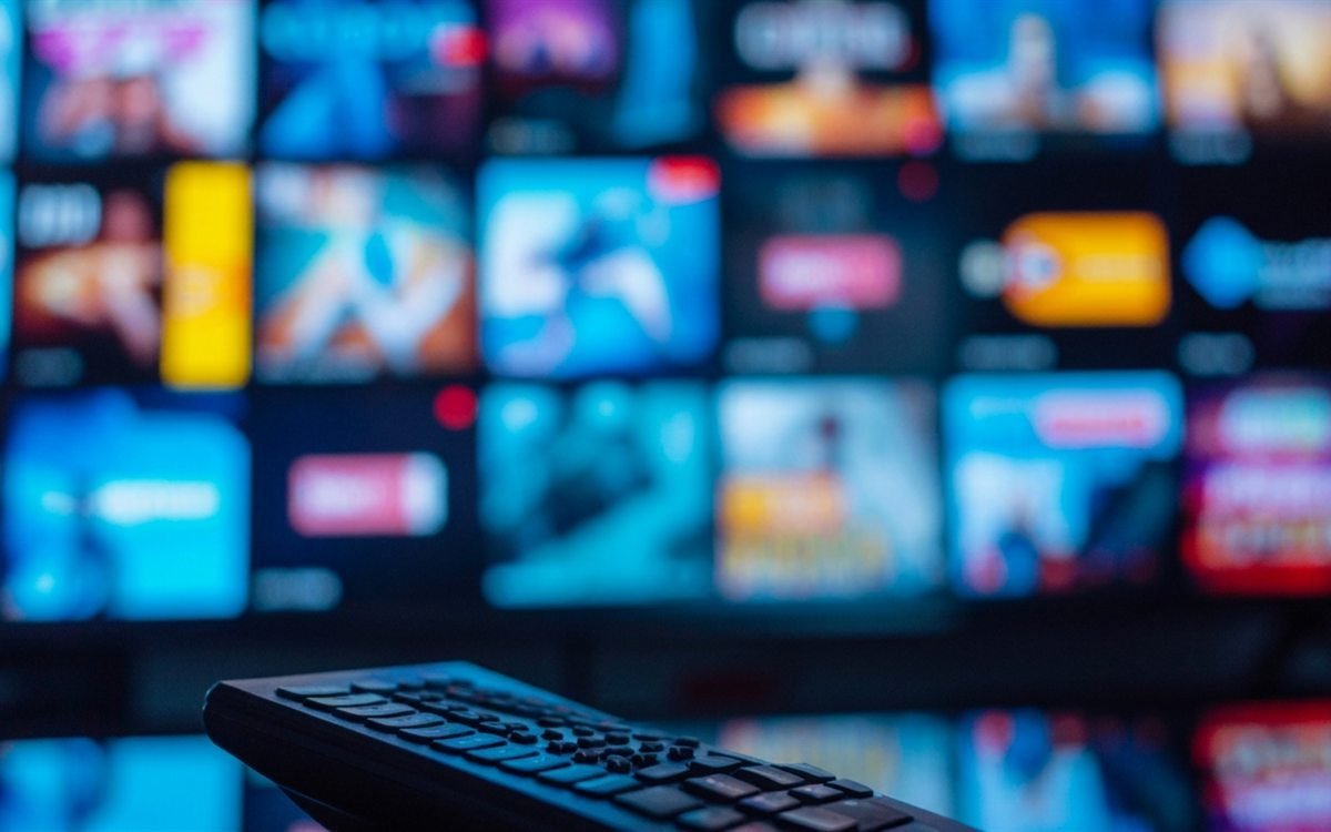 A wall of live TV channels on a Smart TV with a remote in the foreground — 28,000+ IPTV channels available in Australia